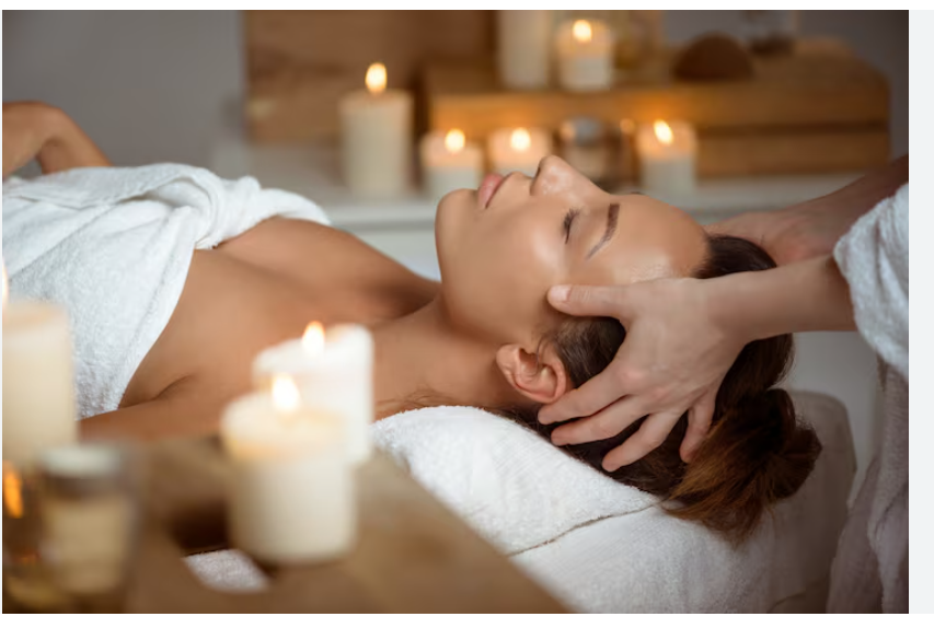 Spa therapist massaging woman's temples/head with candles in foreground